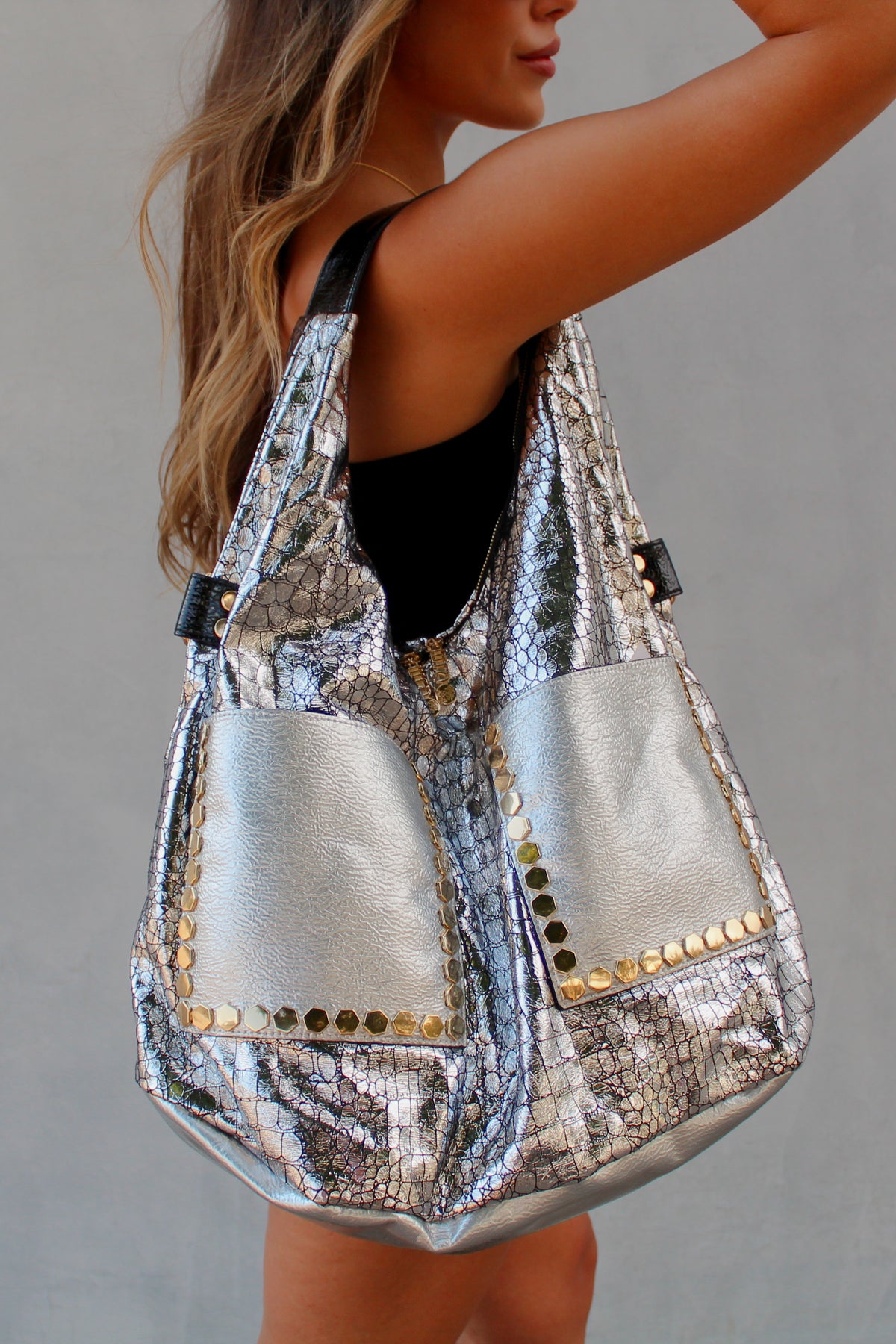 Person holding a silver slouchy studded handbag against a neutral background